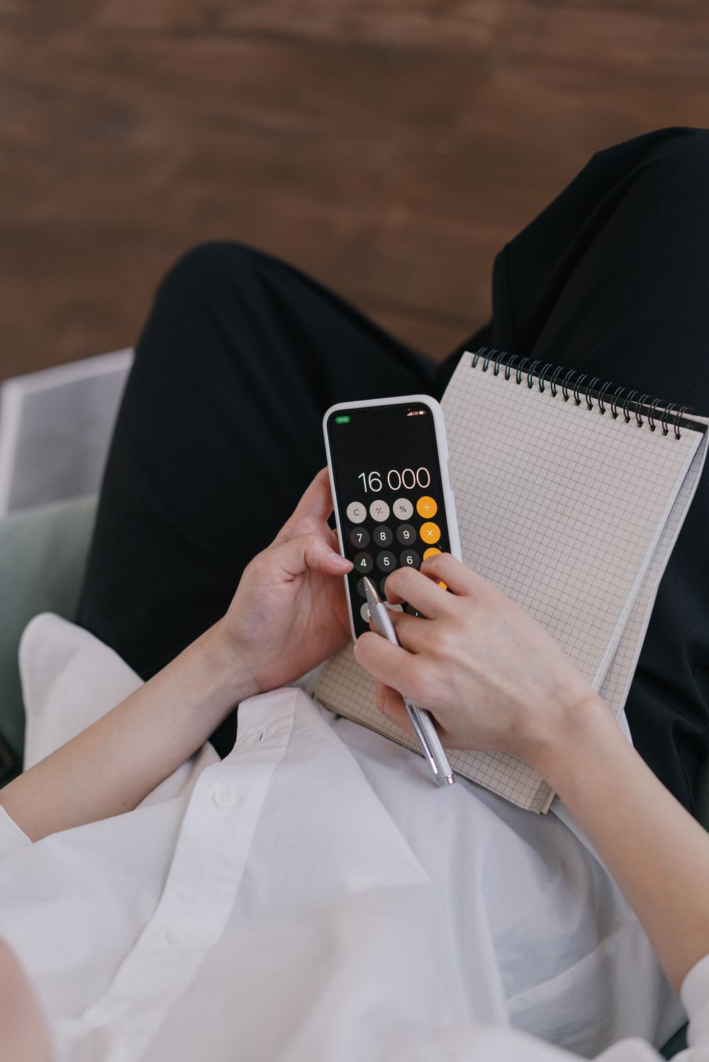 Iemand rekent bedragen uit op een telefoon met een notitieboek op schoot