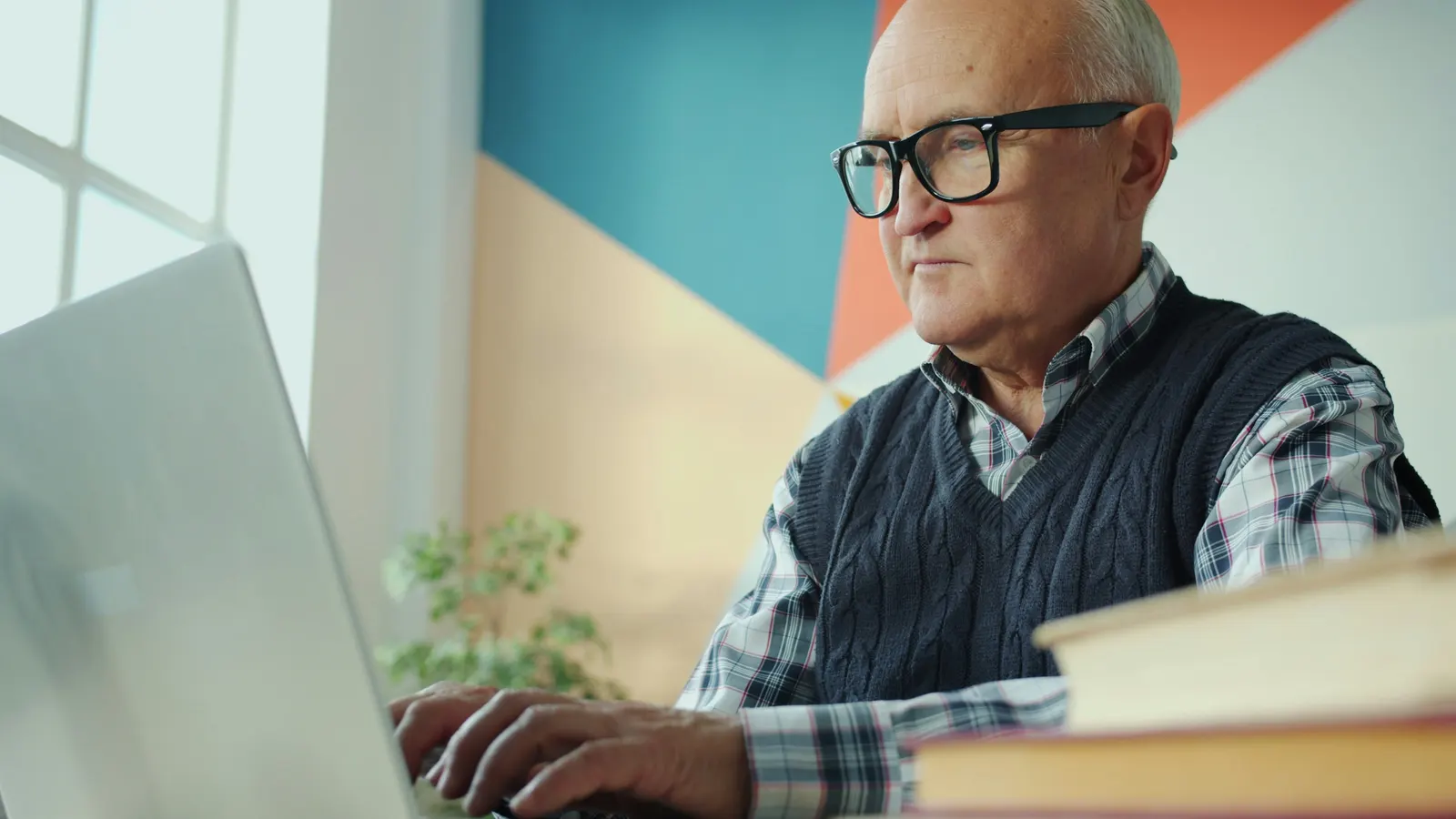 Oudere man met bril zoekt iets op aan zijn laptop